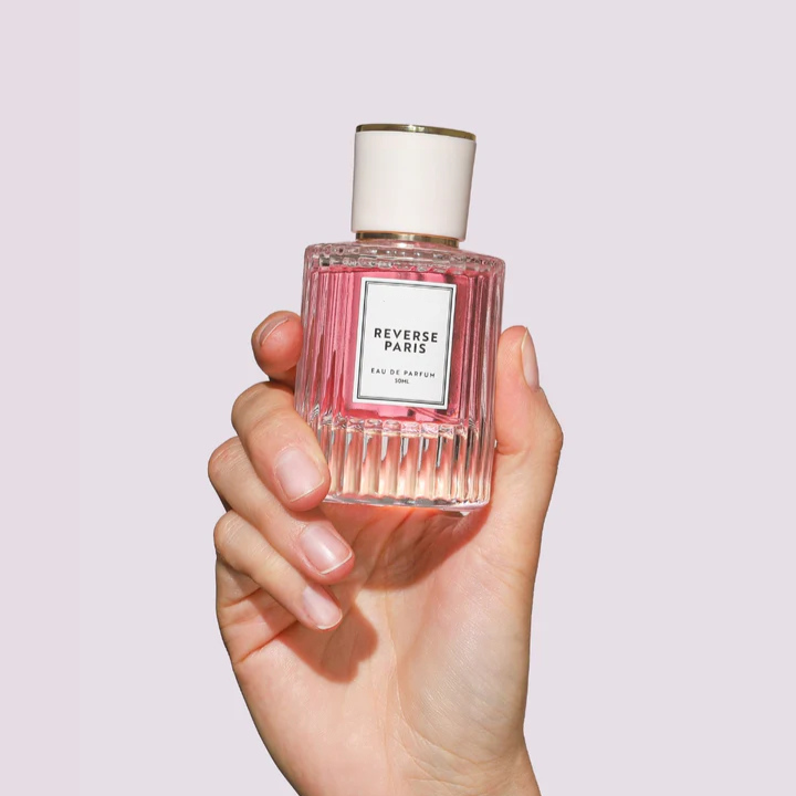 Hand holding a luxurious pink bottle of Reverse Paris Eau de Parfum, 30ml